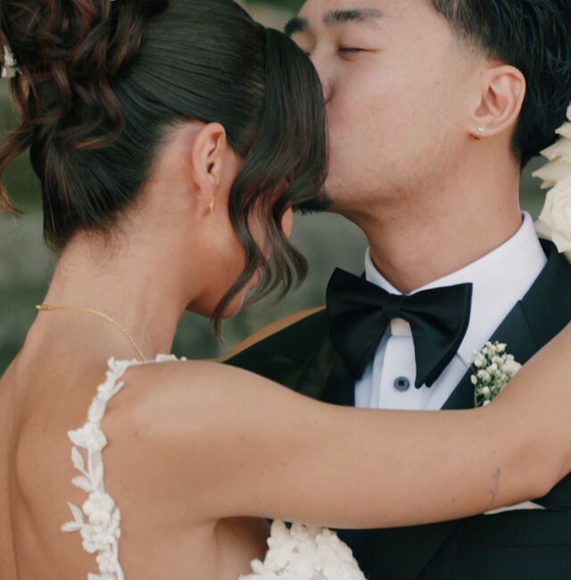 A bride and groom embrace closely at their Whistle Bear wedding; the groom kisses the bride on the forehead. Both wear formal attire, with the bride in a white lace dress and the groom in a black tuxedo.