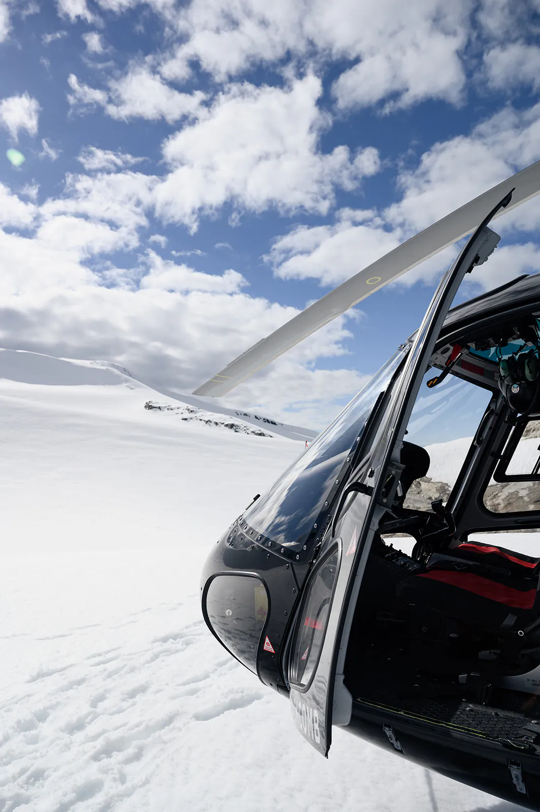 A black helicopter is parked on a snowy landscape under a partly cloudy sky.