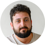 A man with dark hair and beard, wearing a light-colored shirt, looks at the camera against a plain background.